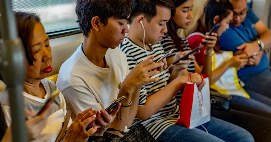 คนหลายวัยนั่งเรียงกันบนรถไฟฟ้า ทุกคนกำลังดูโทรศัพท์มือถือของตัวเอง
