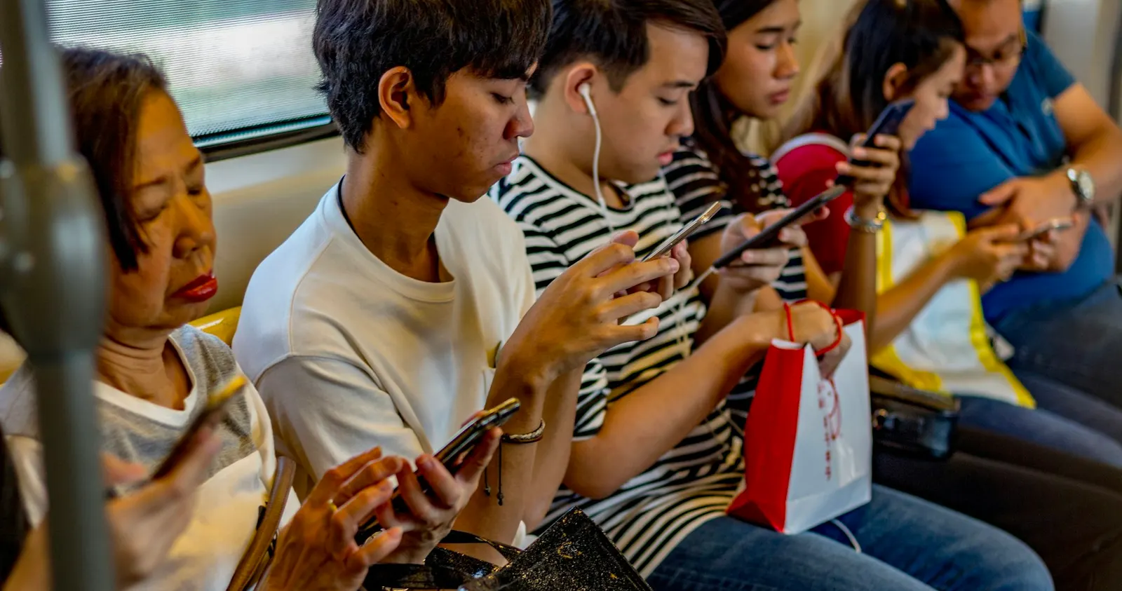คนหลายวัยนั่งเรียงกันบนรถไฟฟ้า ทุกคนกำลังดูโทรศัพท์มือถือของตัวเอง