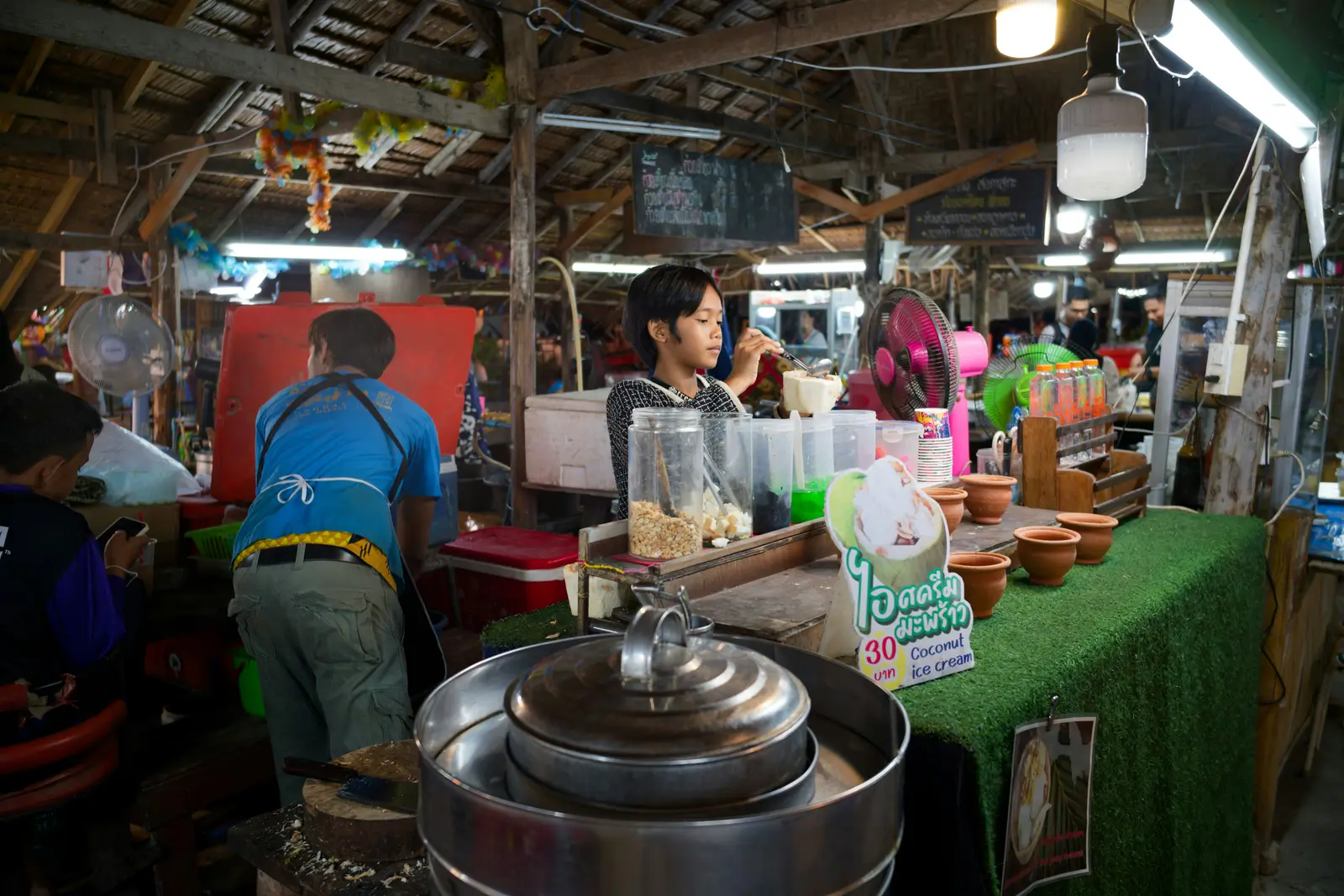 ร้านเครื่องดื่มในตลาดไทย แม่ค้ากำลังทำเครื่องดื่มให้ลูกค้าที่ยืนรออยู่หน้าร้าน